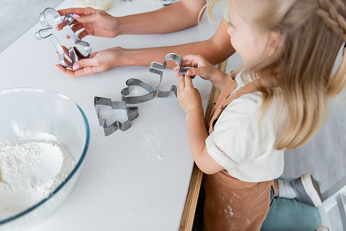 woman showing cookie cutter to blurred daughter in kitchen