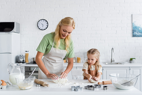 mother and daughter in aprons kneading dough in kitchen