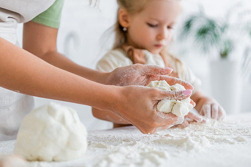 woman kneading dough near blurred daughter in kitchen