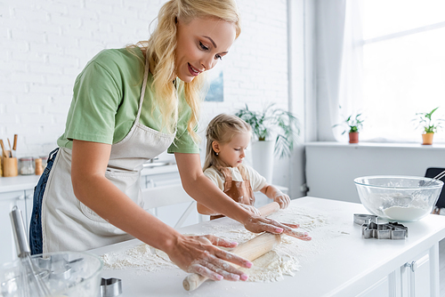 woman with little daughter rolling raw dough on kitchen table