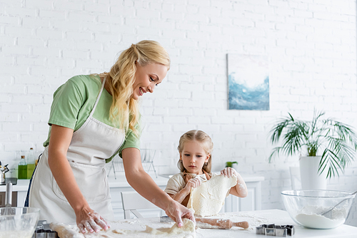 little girl holding raw dough while helping mom in kitchen