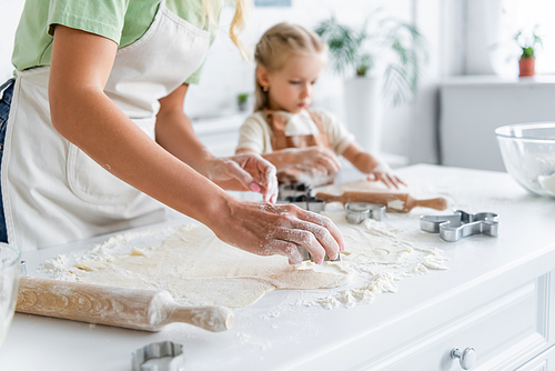 woman cutting dough with cookie cutter near blurred child in kitchen