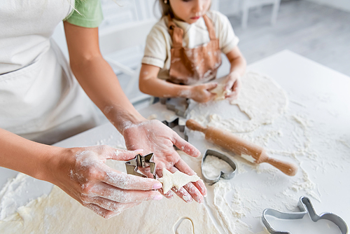 cropped view of woman holding raw fir-shaped cookie near blurred girl in kitchen