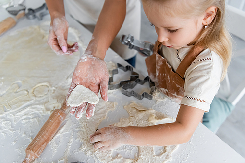 high angle view of woman showing raw heart-shaped cookie to daughter in kitchen