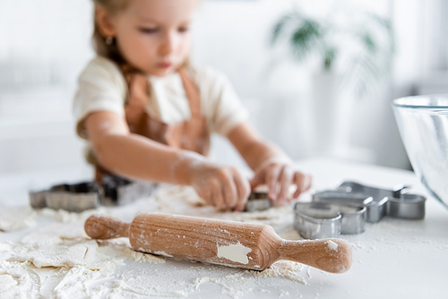 selective focus of rolling pin near blurred girl with cookie cutters