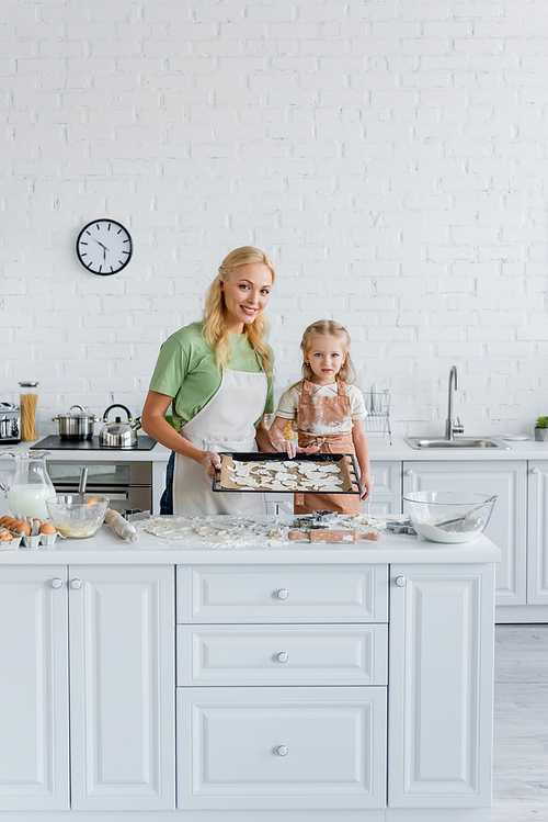 smiling woman with daughter  near baking sheet with raw cookies