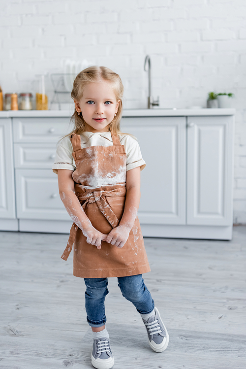 full length view of girl with stains of flour on apron  in kitchen