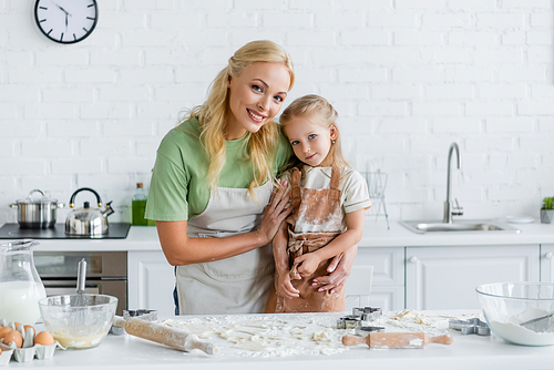 happy woman hugging child near kitchen table with ingredients and cooking utensils