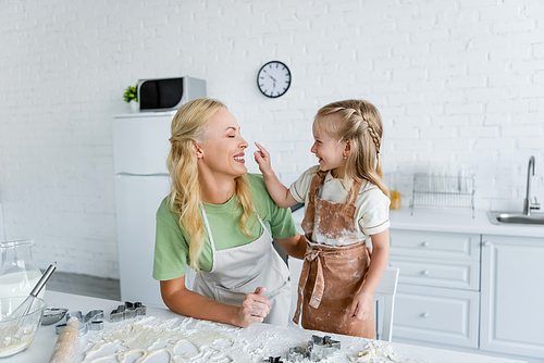 cheerful child touching nose of happy mom while having fun near kitchen table