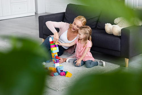 mother and daughter playing with colorful building blocks on floor, blurred foreground