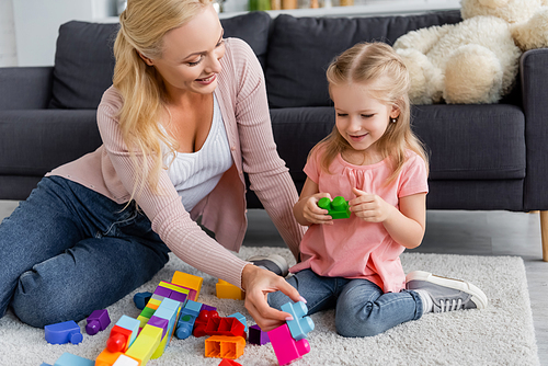 happy woman with smiling daughter playing with multicolored cubes on floor at home