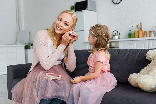 smiling woman putting on earring near daughter in fairy costume