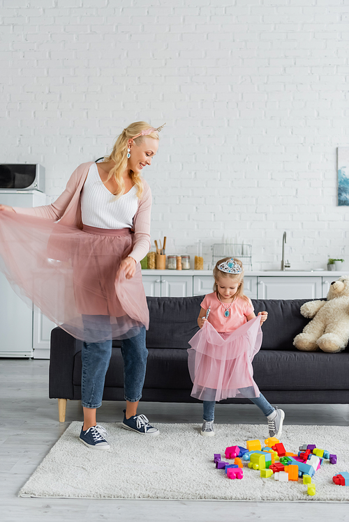 happy woman and girl in tulle skirts and toy crowns dancing in kitchen