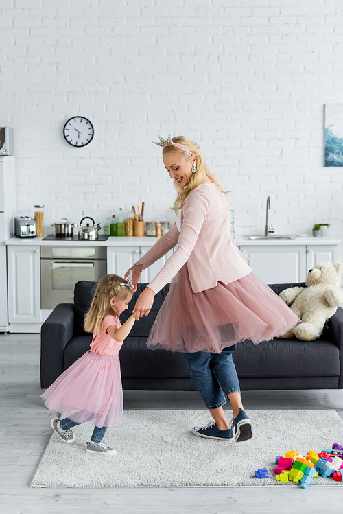 joyful mom and child in fairy costumes holding hands while dancing at home