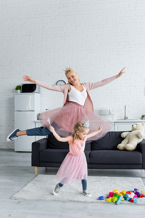 excited woman with daughter dancing at home while wearing costumes of princesses