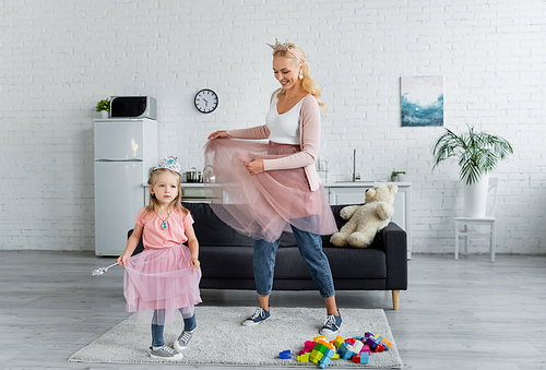 cheerful woman and child in costumes of princesses dancing in kitchen