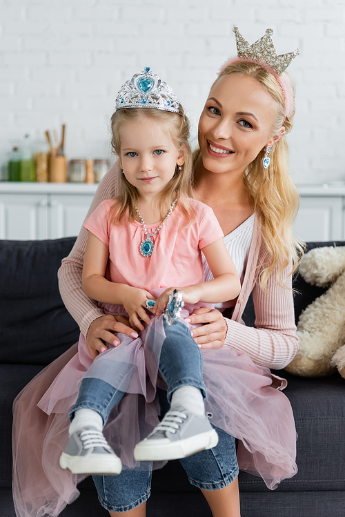 mom and daughter in toy crowns smiling at camera while sitting on couch