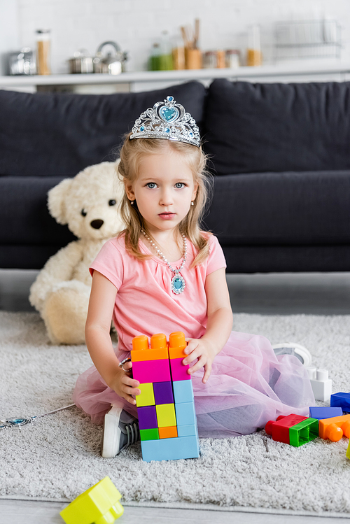 girl in toy crown  near tower of colorful building blocks