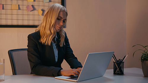 Tired businesswoman using laptop in office in evening
