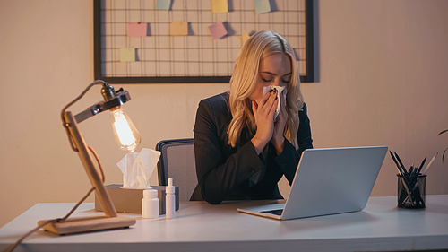 Businesswoman suffering from runny nose near pills and laptop in office
