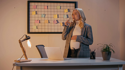 Pregnant businesswoman drinking water in office in evening