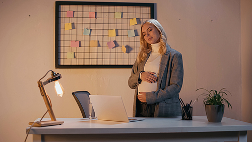 Pregnant businesswoman looking at laptop on office table in evening