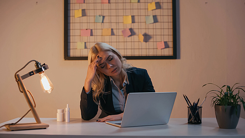 Tired businesswoman sitting near laptop and pills in office