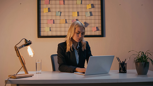 Businesswoman using laptop near lamp in office in evening