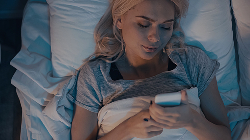 Top view of woman using smartphone while lying on bed