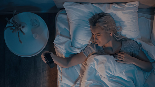 Top view of of woman looking at clock while lying on bed at night