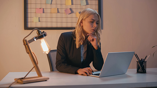 Businesswoman using laptop near lamp on table in office