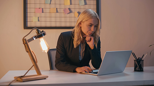 Businesswoman working on laptop near lamp in office in evening