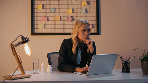 Businesswoman looking away near laptop and pills on office table