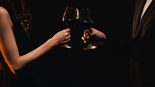 Cropped view of elegant couple toasting with wine glasses isolated on black