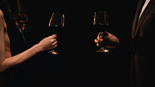 Cropped view of elegant couple holding glasses with red wine isolated on black