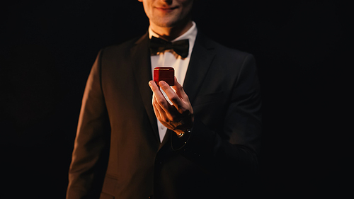 cropped view of man in suit holding red box while making proposal isolated on black