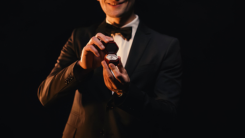 cropped view of happy man in suit holding red box with wedding ring isolated on black