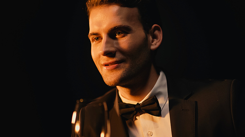 smiling young man in suit with bow tie holding glass isolated on black