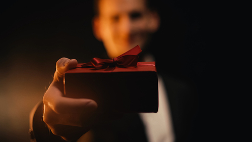 blurred man in suit showing red gift box on black