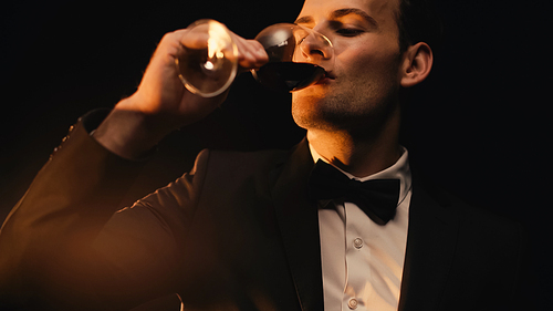 elegant man in suit drinking red wine isolated on black