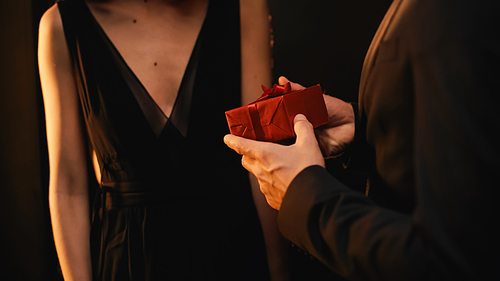 partial view of young man in suit holding red gift box near woman isolated on black