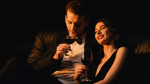 young and happy couple holding glasses of red wine isolated on black