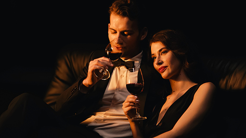 pleased couple holding glasses of red wine isolated on black