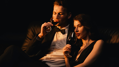 young couple holding glasses and drinking red wine isolated on black