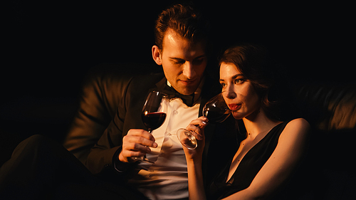 young elegant couple holding glasses of red wine isolated on black