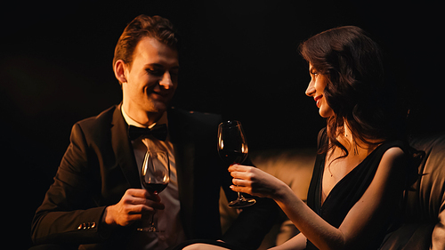 cheerful couple holding glasses of red wine isolated on black
