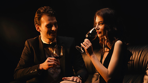 Happy couple holding glasses and drinking red wine isolated on black