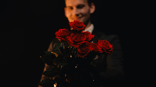happy and blurred man holding red roses isolated on black