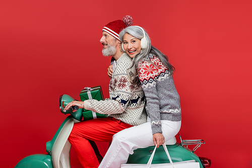 happy and interracial mature couple with christmas presents riding moped on red