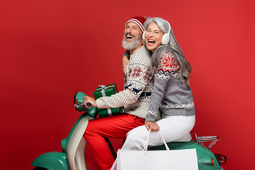 excited and interracial mature couple with christmas presents riding moped on red